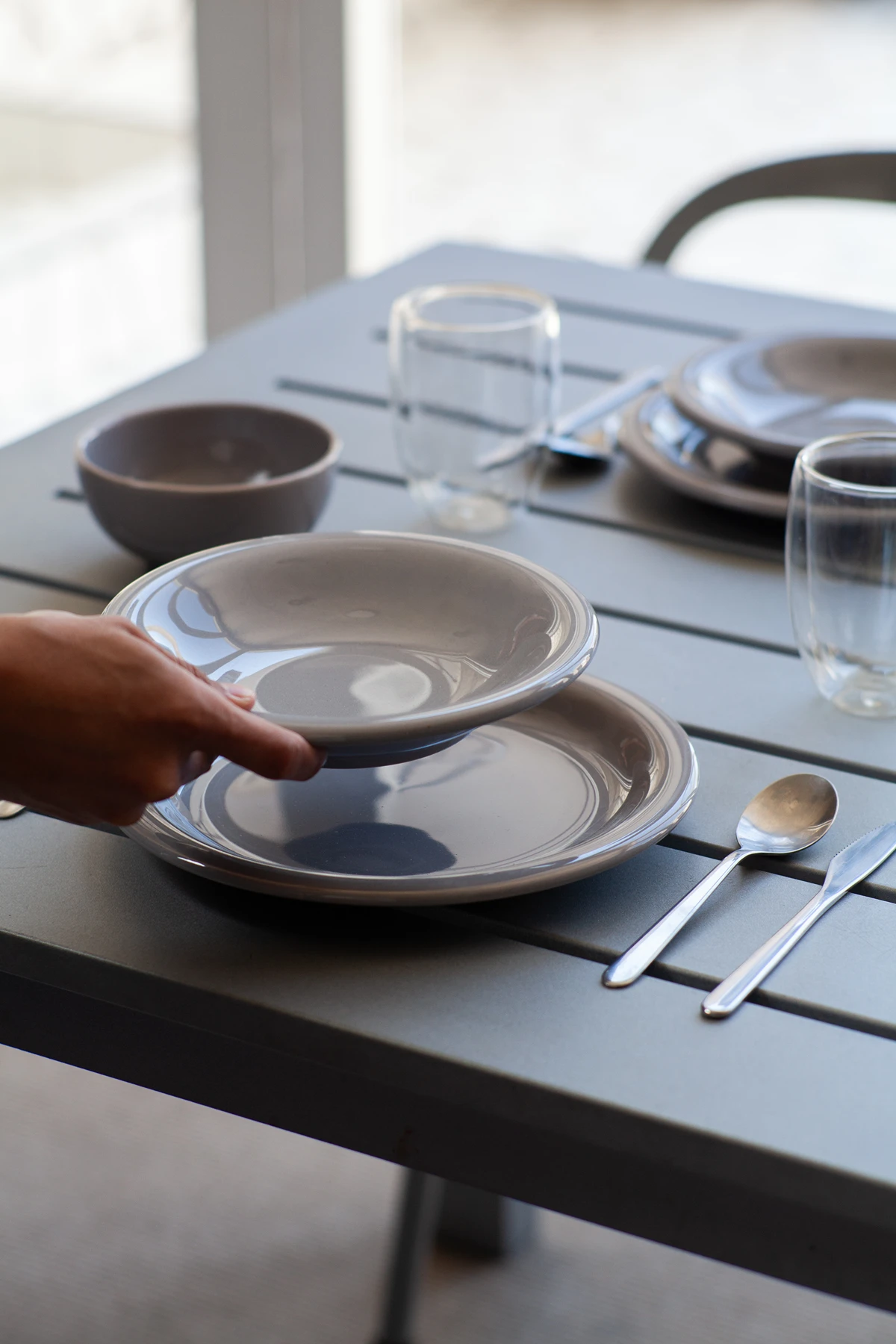 Persona sirviendo la mesa con platos de cerámica color gris fumée